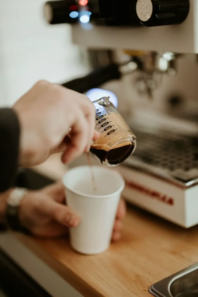 A barista pouring a shot of espresso into a white cup