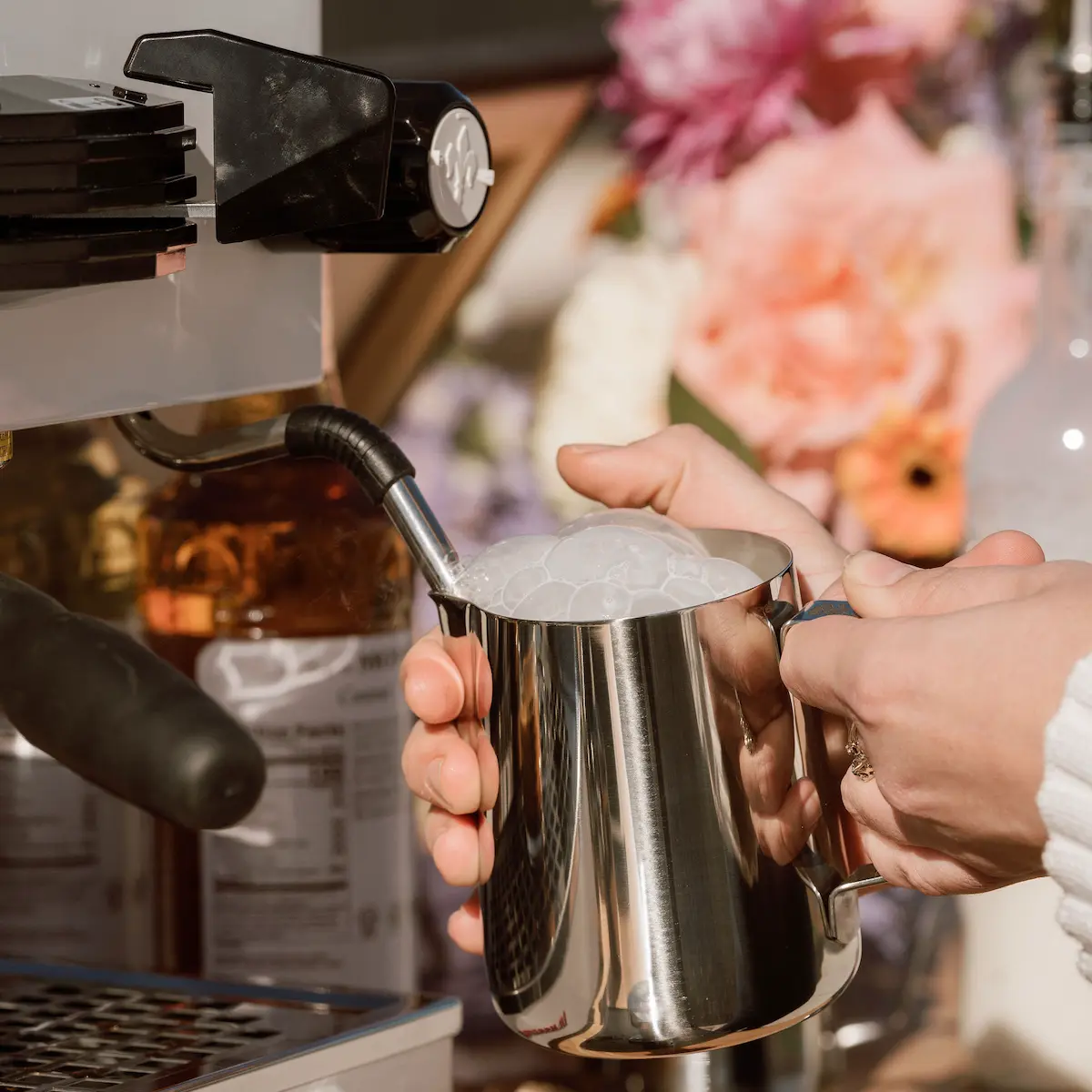 Barista putting steamed milk in a metal cup