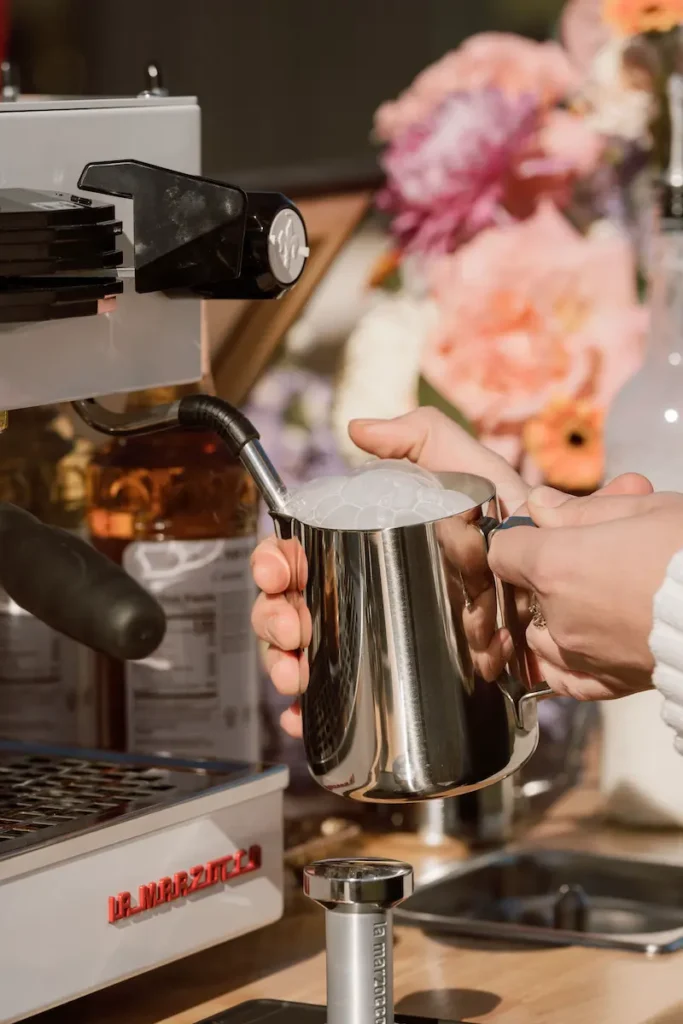 Barista putting steamed milk in a metal cup