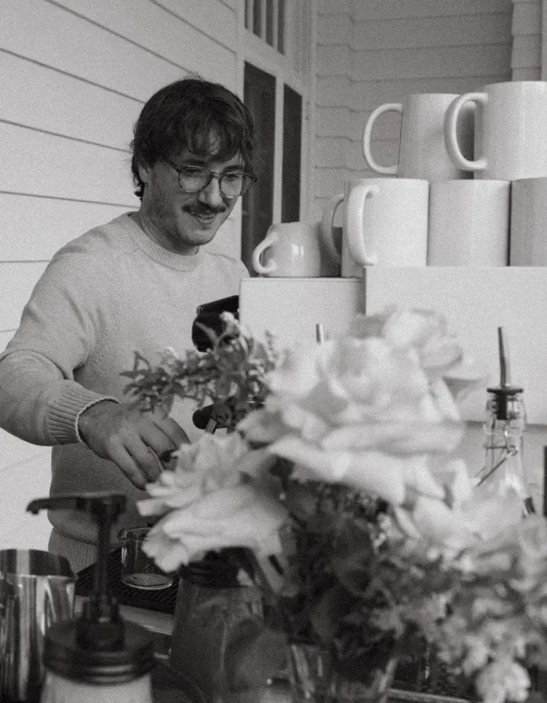 Black and white photo of Zack, co-founder of Roaming Spirits Coffee, making coffee behind a custom mobile espresso cart