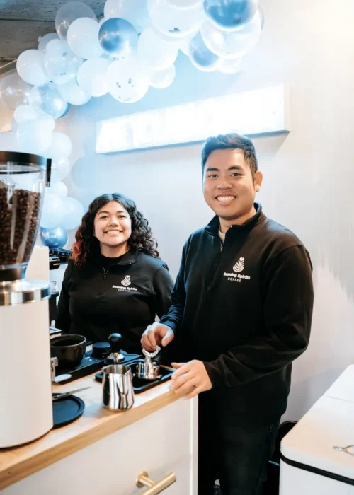 Two baristas standing behind a custom Roaming Spirts Coffee espresso smiling